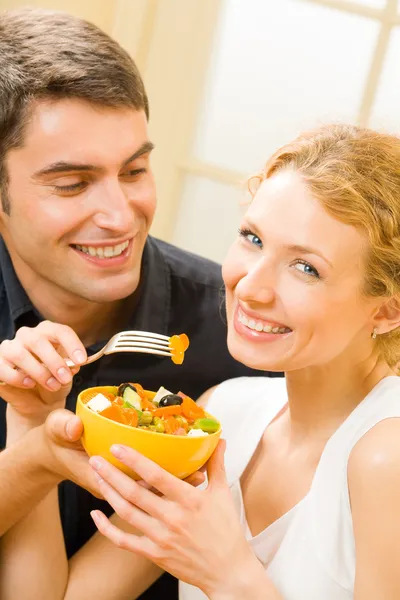 Young happy couple eating salad at home together