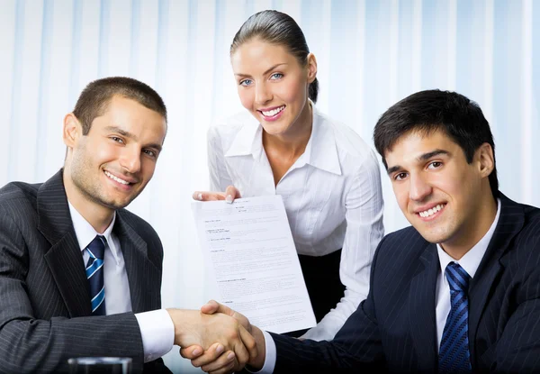 Businesspeople handshaking with document at office