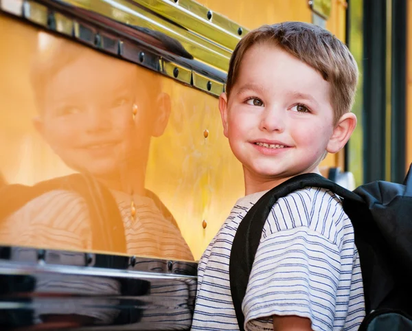 Young boy with nervous smile waits to board bus on first day of school.