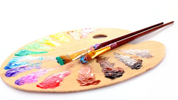 Wooden art palette with blobs of paint and a brush on white back
