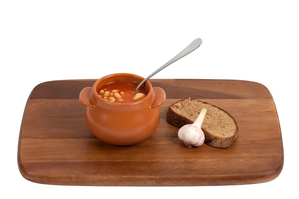Soup in clay pot with bread and garlic on wooden kitchen board. — Stock Photo, Image