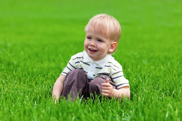 Uśmiechnięty chłopiec siedzi w świeżej trawy — Zdjęcie stockowe