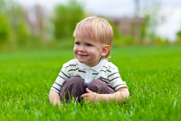 Sorrindo menino sentado na grama fresca — Fotografia de Stock
