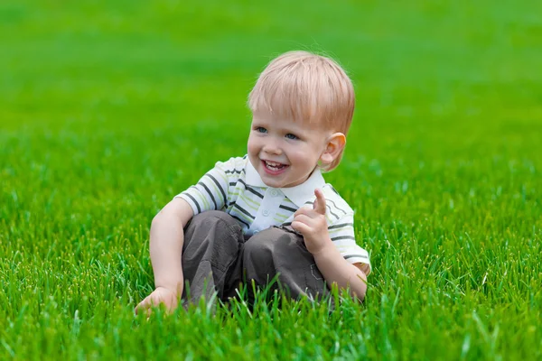 Mały chłopiec siedzi i marzy w zielonej trawie — Zdjęcie stockowe