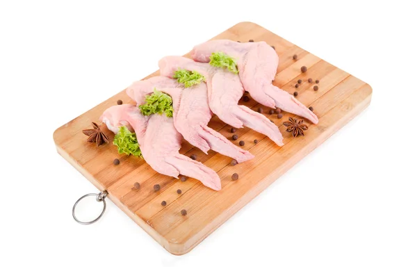Asas de frango cru com condimentos em tábua de madeira — Fotografia de Stock