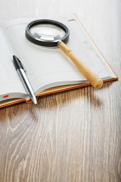 Pen en vergrootglas op notebook — Stockfoto