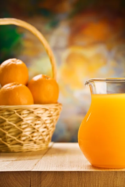 Jug with orange juice and oranges in busket — Stock Photo, Image