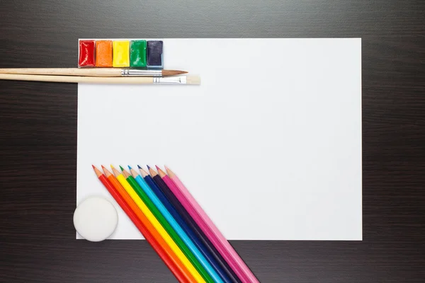 Folha de papel sobre a mesa marrom com tintas coloridas e pencos — Fotografia de Stock