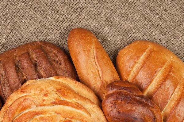 Різноманітність свіжого хліба на тлі мішків — стокове фото