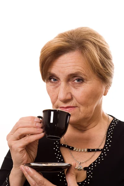 Schöne ältere Frau trinkt Kaffee auf einem weißen — Stockfoto