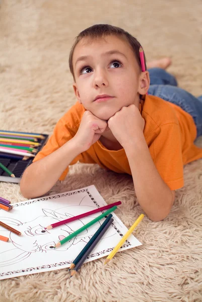 Fundersam unge med pennor på mattan — Stockfoto