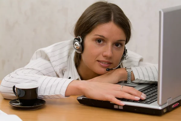 Office girl at the desk with a cup and headset — Stock Photo, Image
