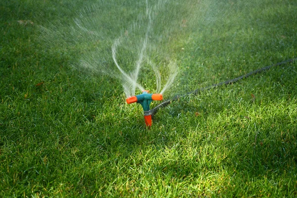 Postřikovač stříká vodu na trávu — Stock fotografie