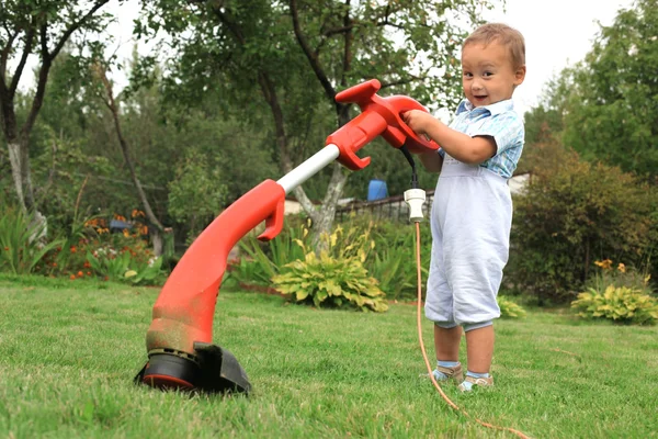 Маленький мальчик с триммером в саду — стоковое фото
