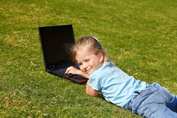 緑の芝生上のラップトップを持つ子供. — ストック写真