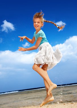 Child playing on beach aganist blue sky. clipart