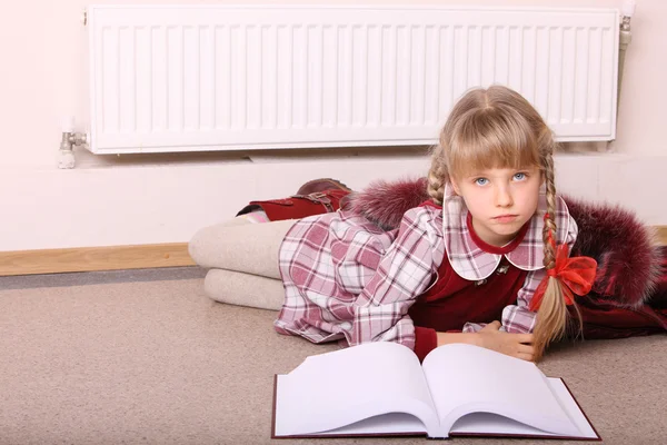 Dziewczyna leżeć na podłodze w pobliżu grzejnika z książki. — Zdjęcie stockowe