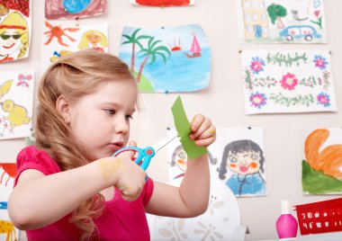 Child with scissors cut paper in play room. clipart