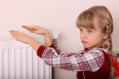 Girl warm one's hands near radiator. Crisis. clipart