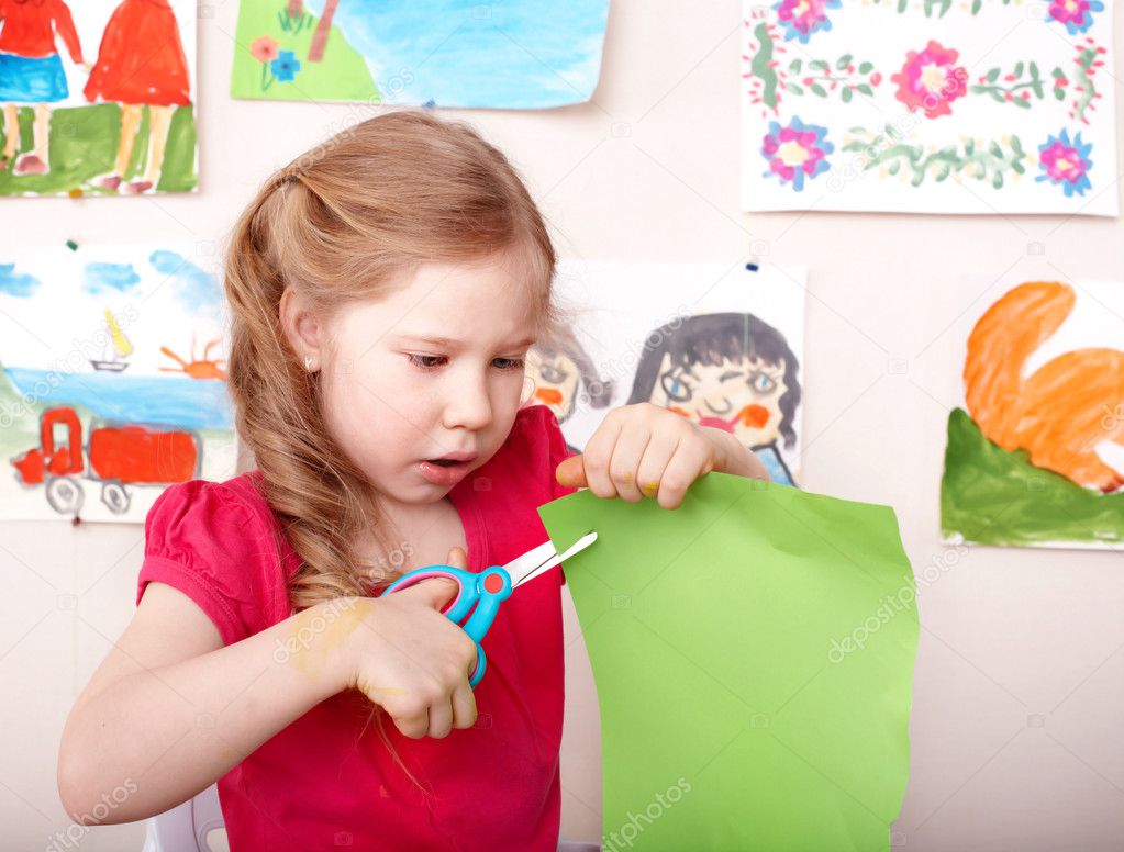 Child with scissors cut paper at home.