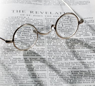 Antique reading glasses on page of bible clipart