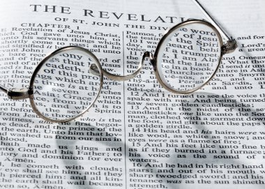 Antique reading glasses on page of bible clipart