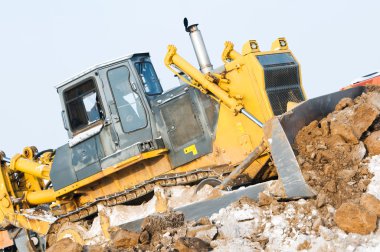 Bulldozer loader at winter frozen soil excavation works clipart