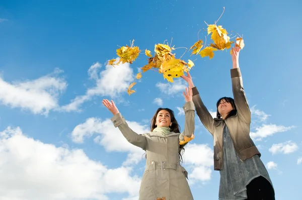 Två flickor och hösten lämnar över blå himmel — Stockfoto