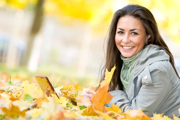 Счастливая студентка лежит в осенних листьях с нетбуком — стоковое фото