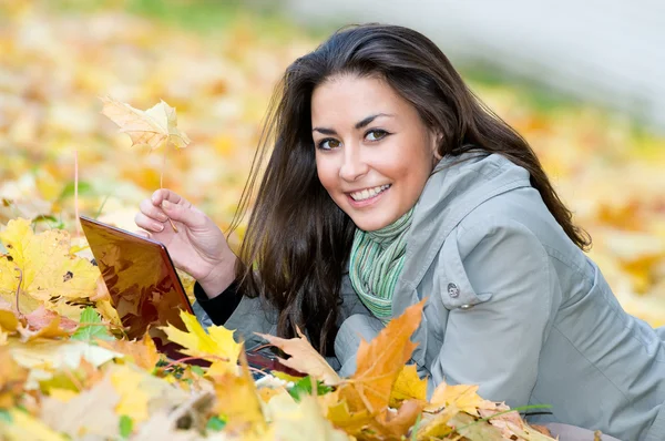 Chica estudiante feliz acostado en hojas de otoño con netbook — Foto de Stock