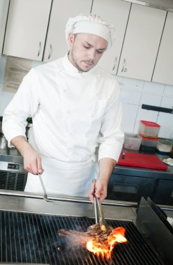 Chef frying beef steak on grill with fire clipart