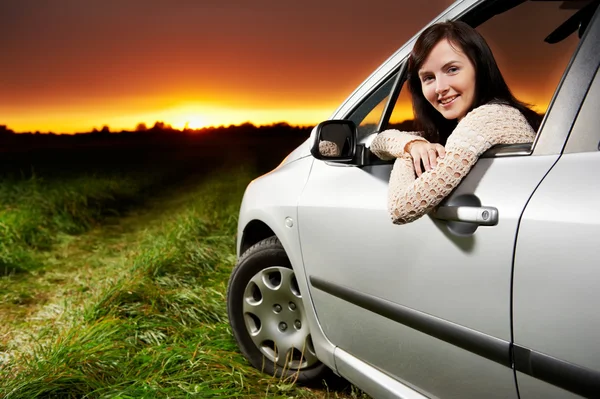 Lachende vrouw in de auto bij zonsondergang — Stockfoto
