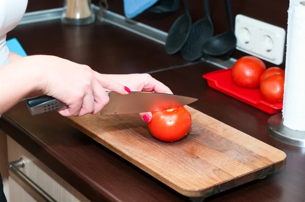 Жіночі руки в інтер'єрі кухні вирізають помідор на обробній дошці — стокове фото