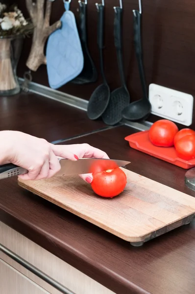 Female hands in kitchen interior cuts a tomato on a cutting board — Stock Photo, Image