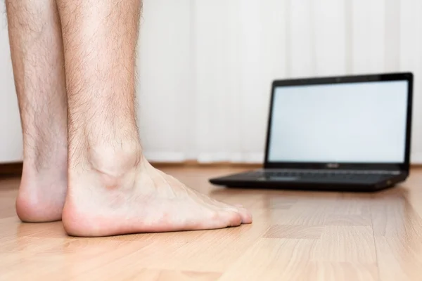 Ordenador portátil abierto y masculinos pies sobre el suelo de parquet —  Fotos de Stock