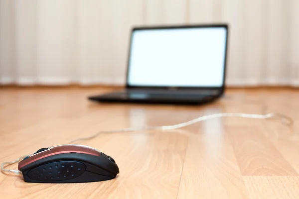 Laptop aberto e um mouse de computador no chão da sala — Fotografia de Stock