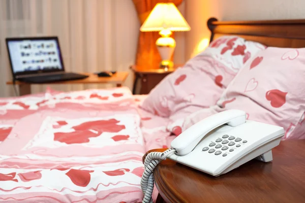 Интерьер спальни с телефоном и ноутбуком рядом с кроватью на столе — стоковое фото