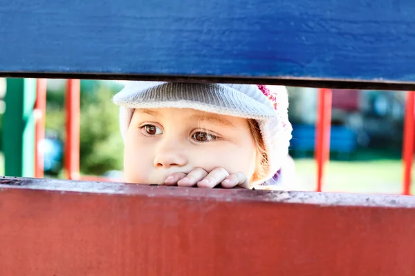 Criança olhando através de uma rachadura entre tábuas de madeira — Fotografia de Stock