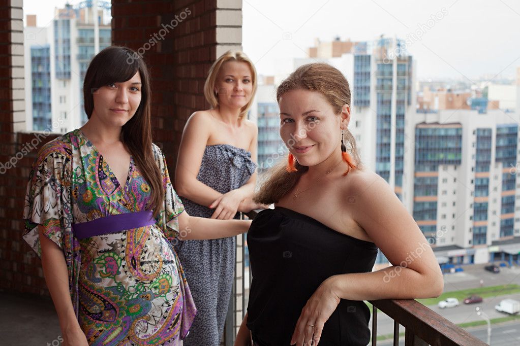 Three young Caucasian women standing on balcony of city high-rise building