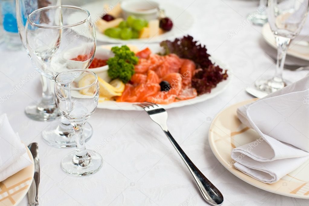 Plates with cold snack on table, cutlery for dinner, white napkin, selective focus.