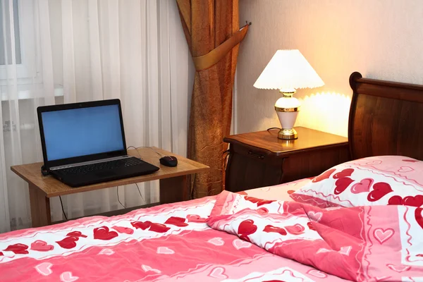 Laptop na mesa perto da cama no quarto — Fotografia de Stock