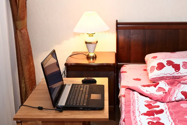 Yatak odasında yatağın yanında masa üstünde laptop — Stok fotoğraf