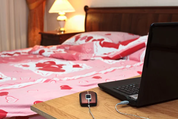 Ordenador portátil en la mesa cerca de la cama en el dormitorio —  Fotos de Stock