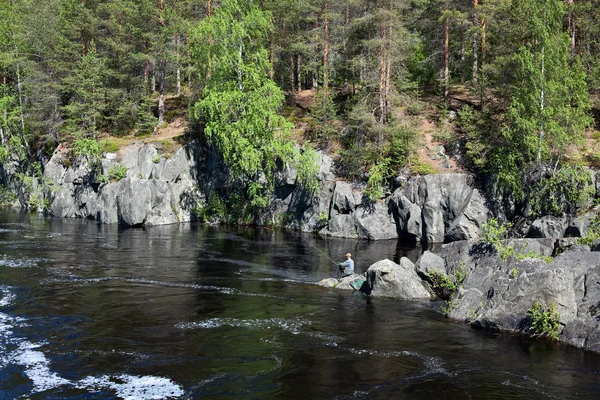 Fisherman sitting on the rocks in mountain river. — Stock Photo, Image