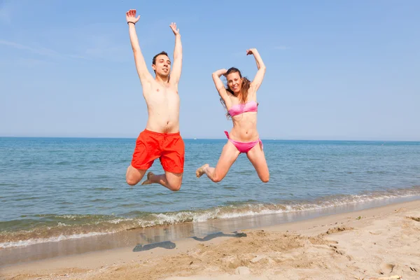Casal feliz pulando na praia no litoral — Fotografia de Stock