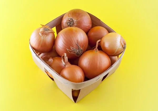 Onions in box on yellow background. — Stock Photo, Image