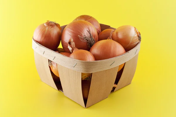 Onions in a box on yellow background. — Stock Photo, Image