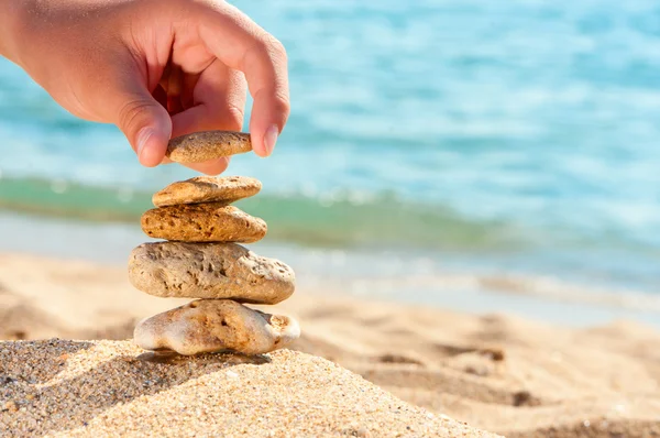 Stone tower on sand with hand against sea.