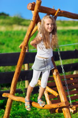 Cute little girl with blond long hair playing on wooden chain sw clipart