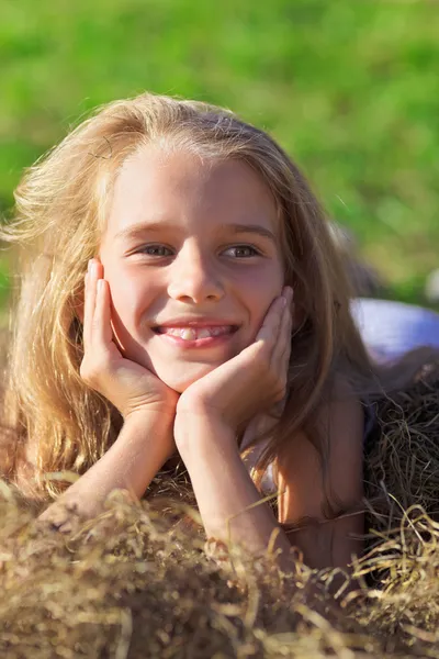 Милая маленькая девочка с светлыми волосами, валяющаяся в куче сена по зеленому закону — стоковое фото